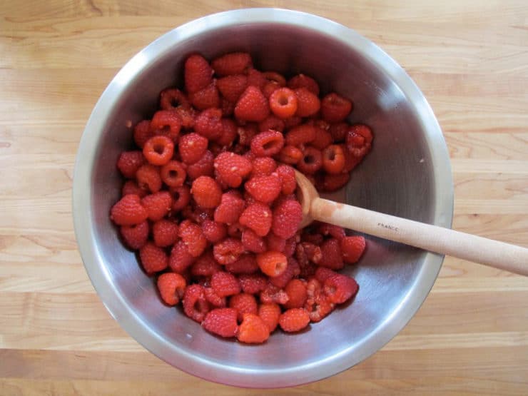 Stirring lemon juice into a bowl of raspberries.