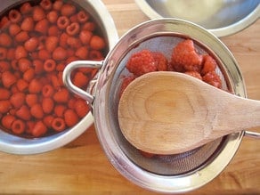 Using a wood spoon to get all liquid out of raspberries.