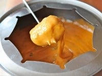 A stick with food dipping into a bowl of Cheesey Jalapeño Fondue, a delicious orange sauce