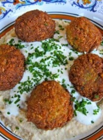 Close up shot of golden-brown falafel balls served with a side of tahini sauce and fresh vegetables