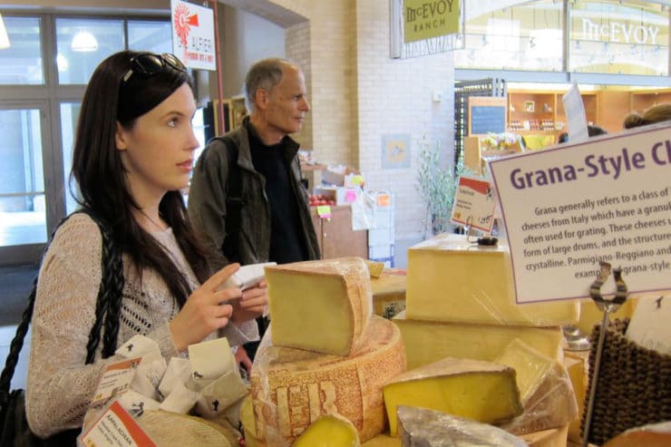 Tori Avey standing at cheese counter at Ferry Plaza Farmer's Market, shopper in background.