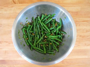 Tossing green beans with dressing in a bowl.