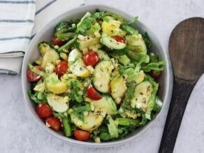 Overhead image - a white bowl filled with grilled vegetable salad, a mix of grilled zucchini, squash, asparagus, corn, tomatoes, lettuce and basil with lemony basil dressing.