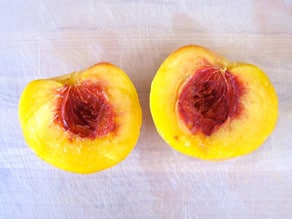 Halved peach on a cutting board.