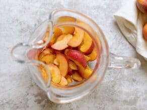 Overhead shot of glass pitcher with sliced peaches sitting at the bottom.