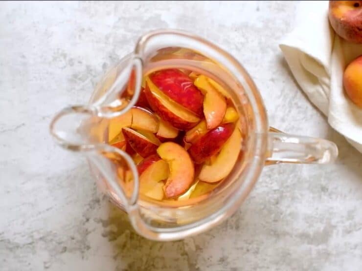 Overhead shot of glass pitcher filled with peach sangria and sliced peaches.