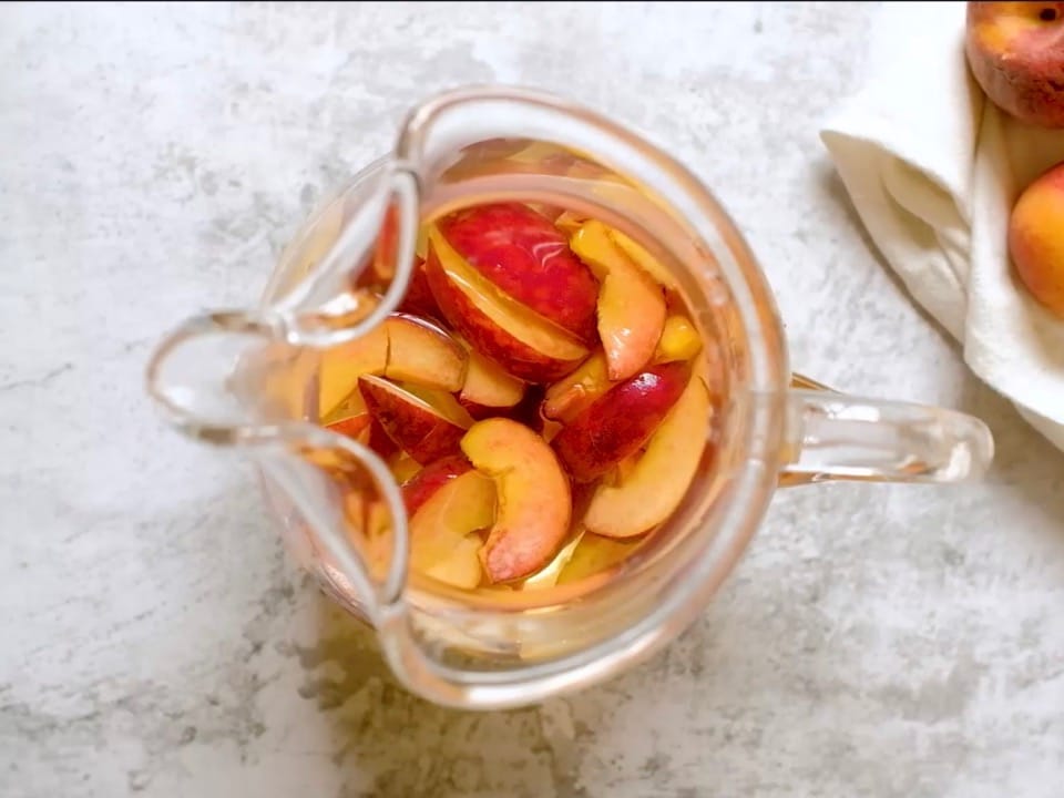 Overhead shot of glass pitcher filled with peach sangria and sliced peaches.