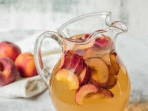 Close up shot of glass pitcher filled with peach sangria and sliced peaches.
