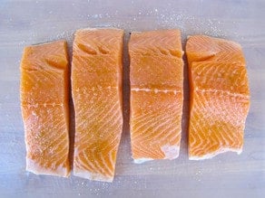 Seasoning salmon fillets on a cutting board.