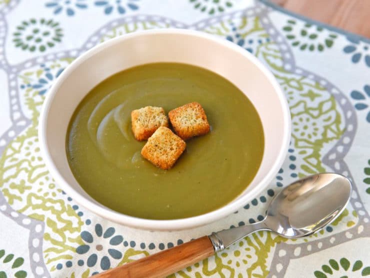 Andersen's Famous Split Pea Soup served on a white bowl topped with three croutons and a spoon on the side