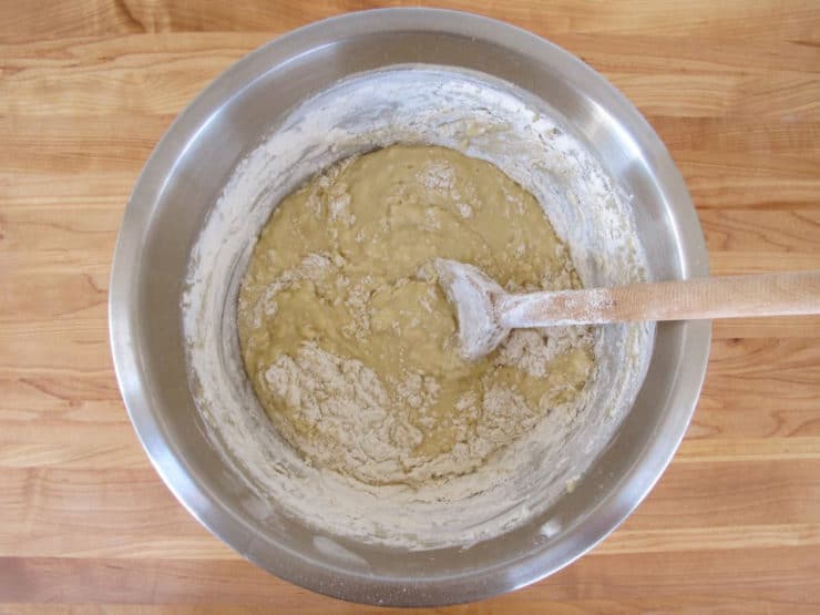 Adding flour to yeast in a bowl.