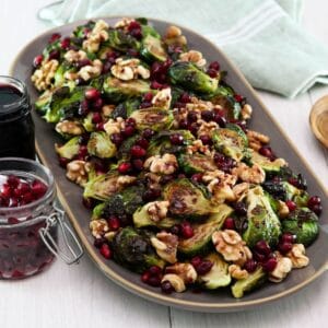 Horizontal shot of a platter filled with roasted brussels sprouts topped with pomegranate molasses.