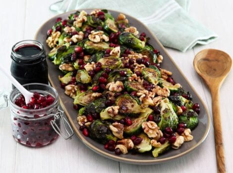 Horizontal shot of a platter filled with roasted brussels sprouts topped with pomegranate molasses.