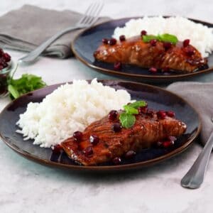 Horizontal shot of two plates holding pomegranate glazed salmon next to a serving of white rice.