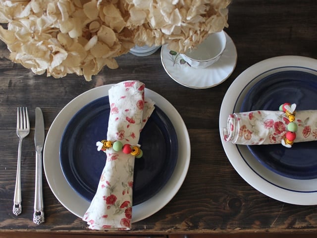 Rosh Hashanah napkin rings in a rolled napkin that is on top of an arranged plates with spoon and fork on the side