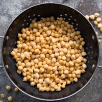 A colander filled with cooked chickpeas on a grey background.
