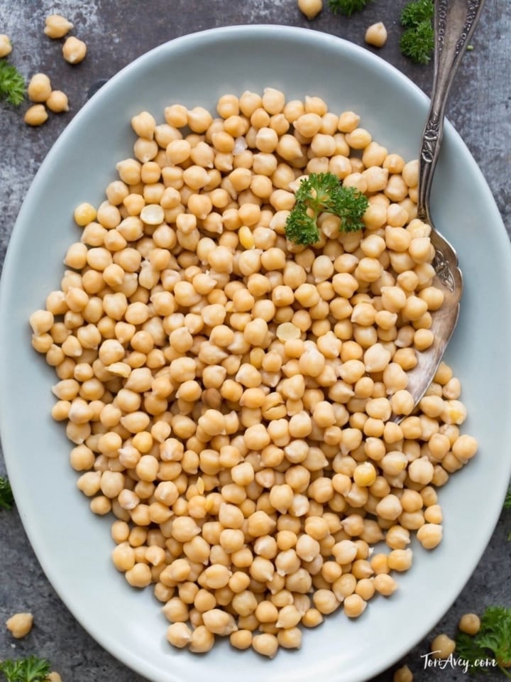 Overhead shot of cooked chickpeas on blue plate with parsley and spoon.