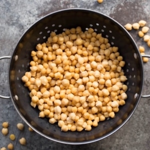 Overhead shot of cooked chickpeas in colander on a grey background.
