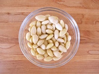 Blanched skinned almonds in glass bowl on wooden cutting board.