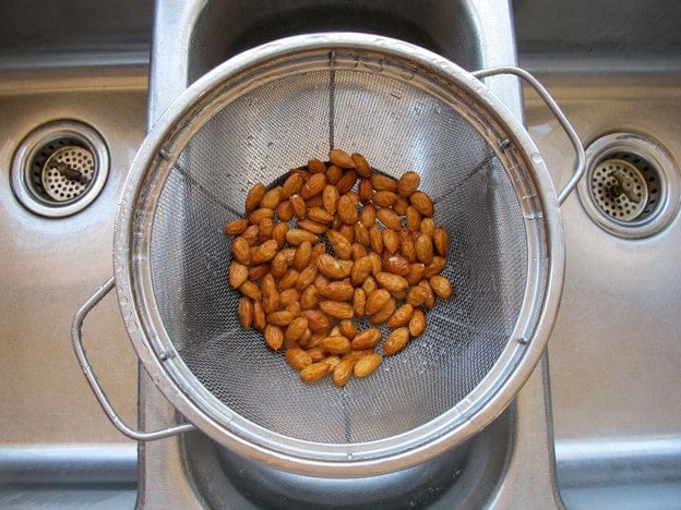 Overhead shot of wet almonds draining in mesh strainer colander.