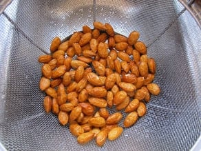 Wet almonds draining in mesh strainer colander, close up - almond skins slightly shriveled.