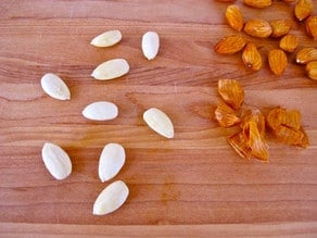 Nine skinned almonds with loose skins beside them, pile of un-skinned almonds on the side.