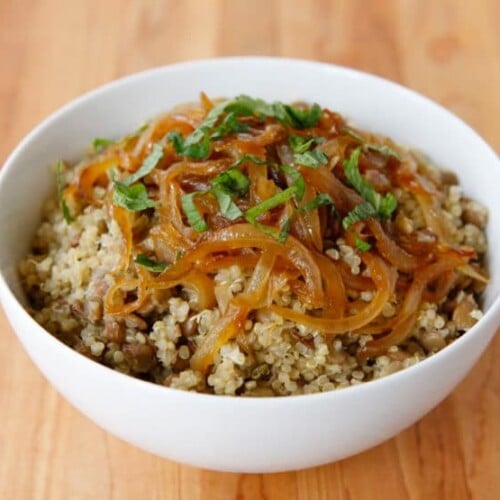 Quinoa Mujadara dish topped with vegetables served in a white bowl on a wooden table