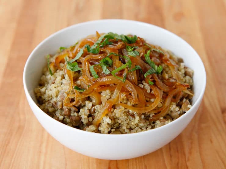 Quinoa Mujadara dish topped with vegetables served in a white bowl on a wooden table