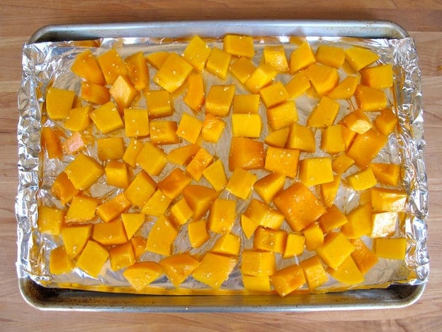 Butternut squash cubes on a foil lined baking sheet.