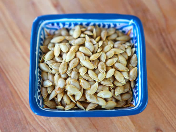 Toasted butternut squash seeds in a blue decorative dish on a wood cutting board.
