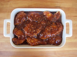 Barbecue sauce poured over chicken in a baking dish.