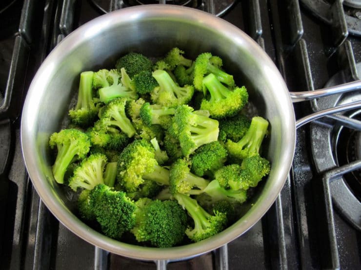 Broccoli florets steaming on the stovetop.