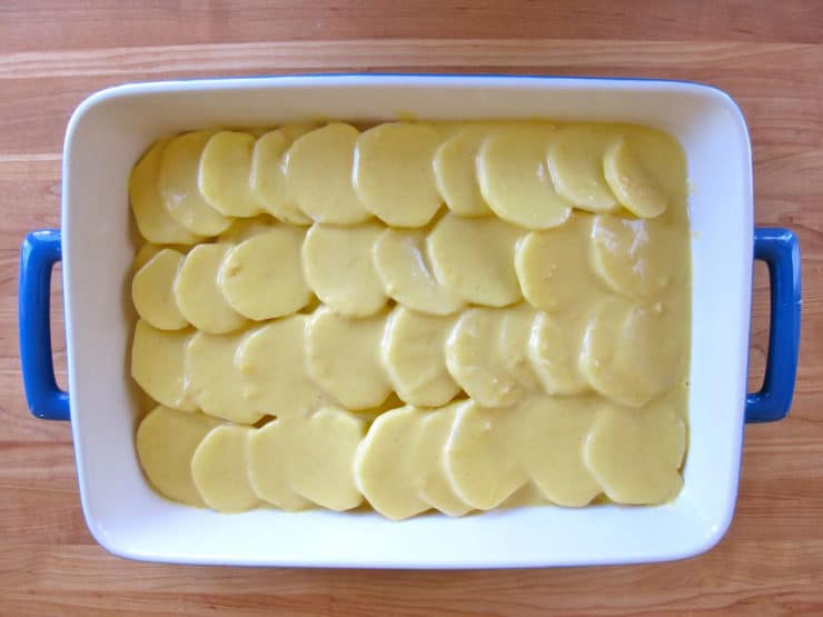 Sauce poured over sliced potatoes in a baking dish.