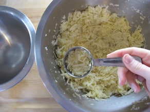 Scooping shredded potatoes with a Tablespoon.