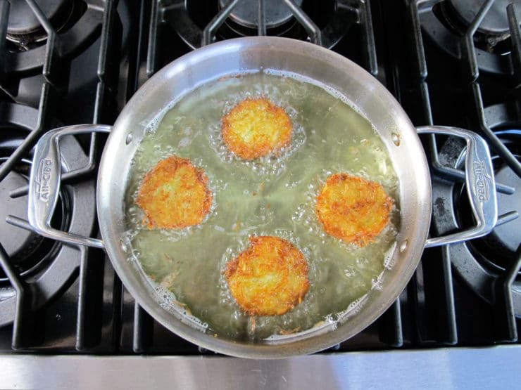 Golden latkes frying on stovetop in stainless steel pan.