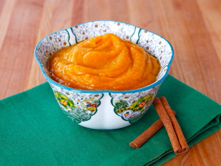 Maple Butternut Squash Puree served in a fancy bowl on top of a green clothe with two cinnamon sticks on the side