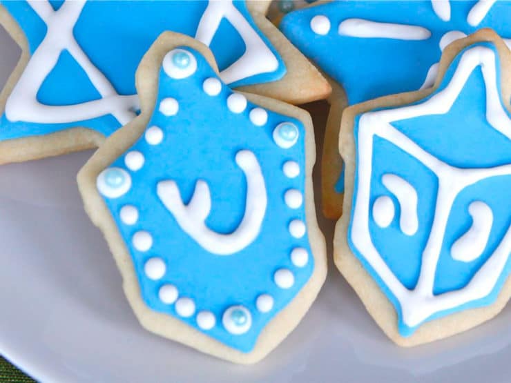 Close up on dreidel-shaped cookie decorated with royal icing and blue candy beads.