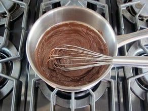 Whisking sugar and butter into melted chocolate.