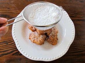 Dusting fritters with powdered sugar.