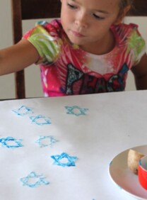 Young girl stamping Hanukkah wrapping paper with star of David potato stamp.