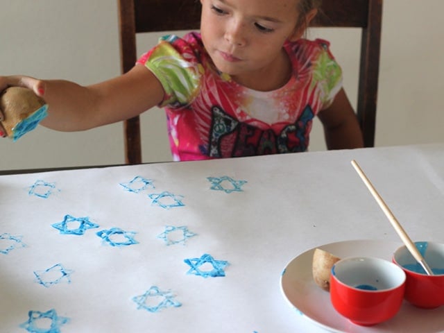 Young girl stamping Hanukkah wrapping paper with star of David potato stamp.