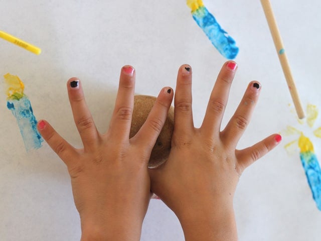 Young girl's hands holding potato stamp over paper.