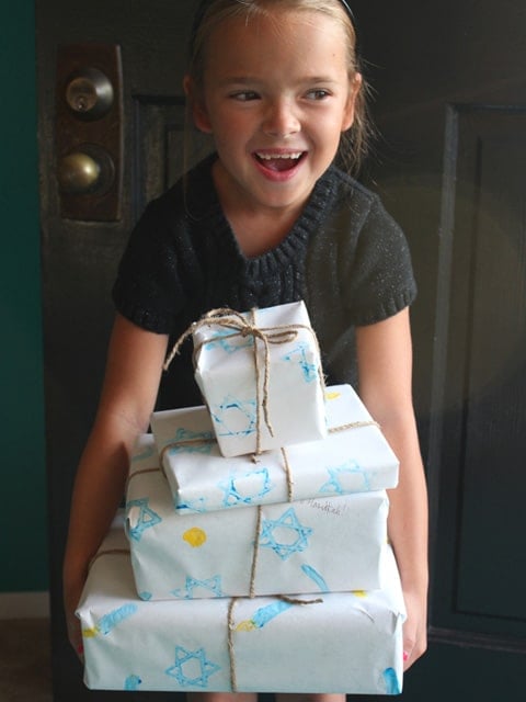 Girl smiling holding gifts wrapped in homemade Hanukkah gift wrap.