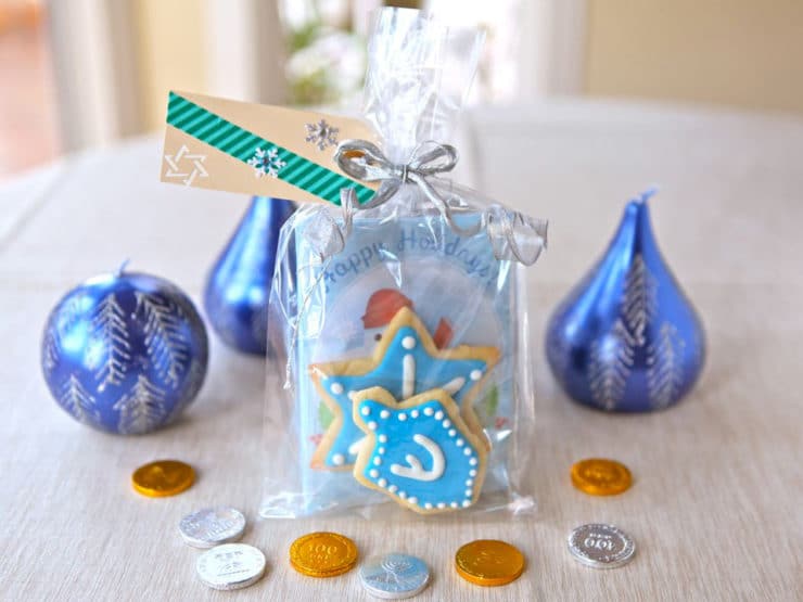 Fully assembled Homemade Cookies and Hot Cocoa Gift Bag on table surrounded by blue holiday candles and gelt.