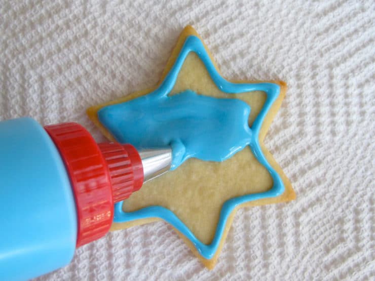 Decorating star of David sugar cookie. Flooding outline with blue icing.