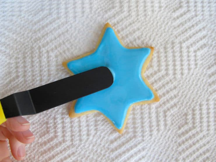 Decorating star of David sugar cookie. Smoothing surface of blue icing with small spatula.