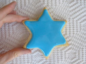 Decorating star of David sugar cookie. Fingers holding cookie edges.