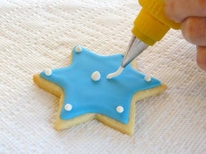 White royal icing dot details being added to blue Jewish holiday sugar cookie.