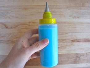 Hand holding icing bottle filled with blue icing topped with metal decorating tip.
