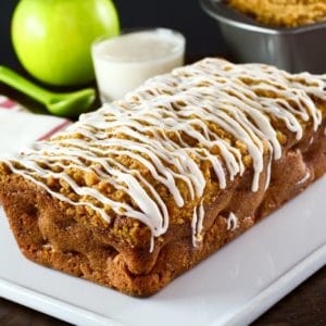 Greek Yogurt Apple Streusel Cake unsliced on white plate with cloth napkins, dish of yogurt, spook and green apple in background.